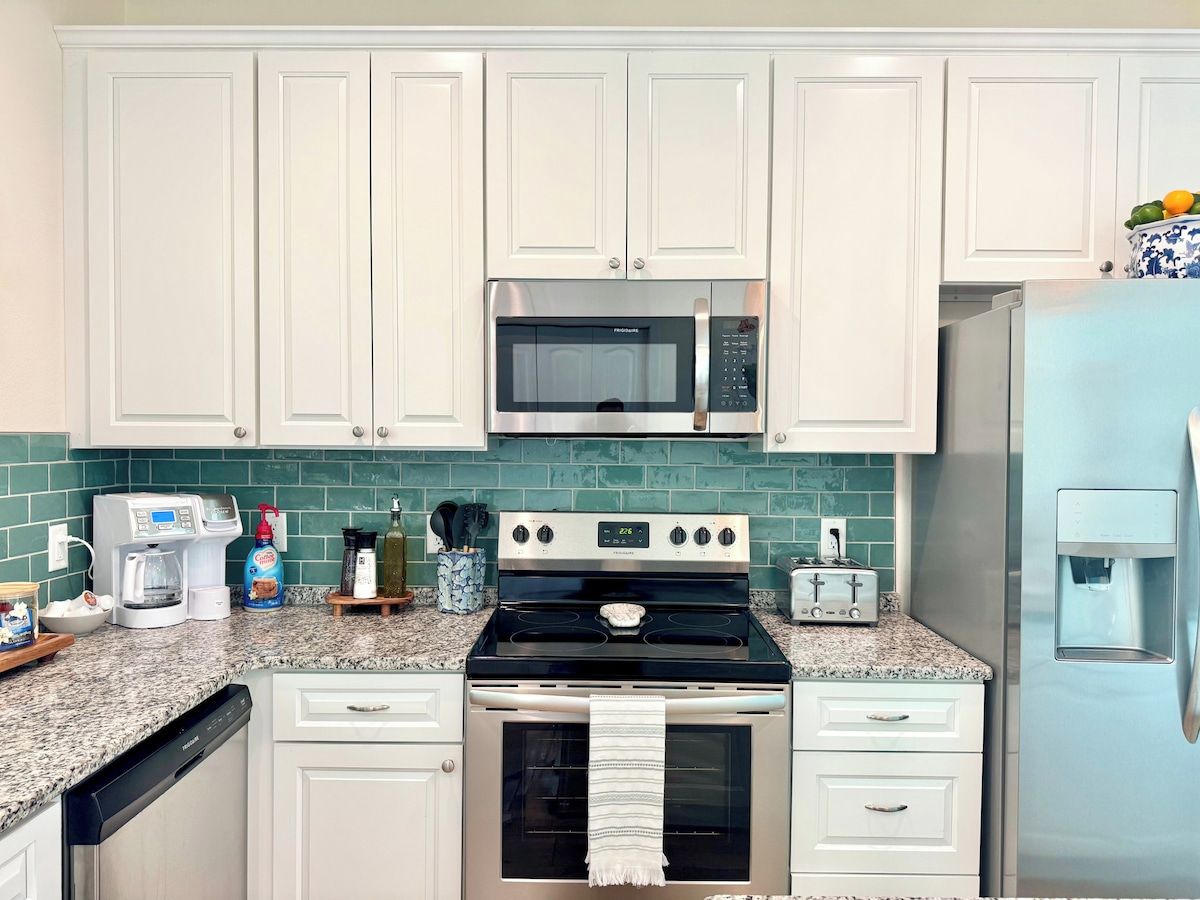 A kitchen with white cabinets, a microwave, a stove, a toaster, and a refrigerator.