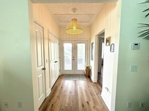 A hallway with wooden flooring, white doors, and a hanging light fixture.