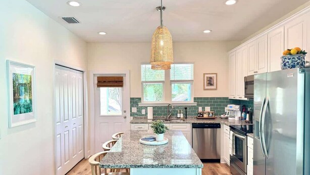 A modern kitchen with a granite countertop, stainless steel appliances, and a hanging light fixture. - The Royal Cypress Suite, Near UF, Shands, Downtown (Gainesville)