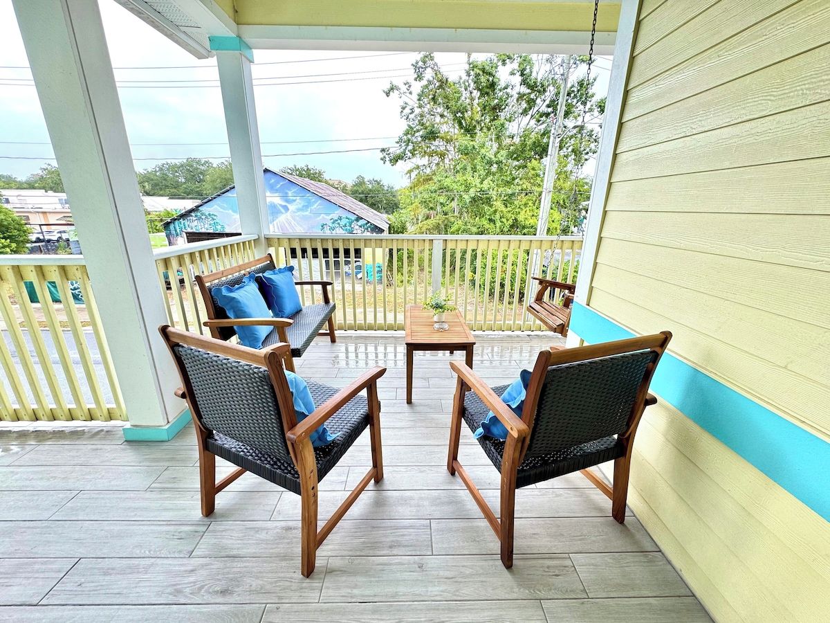 A covered outdoor seating area with two wooden chairs and a small table, surrounded by a wooden fence.