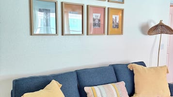 Un canapé bleu agrémenté de coussins jaunes et à motifs, un mur orné de tableaux encadrés et une lampe sur pied.