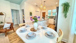 A modern dining area with a round table set for six, a vase of flowers, and a kitchen in the background. - The Royal Cypress Suite, Near UF, Shands, Downtown (Gainesville)