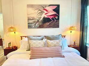 Una habitación de hotel con una cama grande, dos mesitas de noche, una lámpara de noche, un cuadro de un flamenco y dos lámparas de pared.