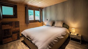 A bedroom with a large bed, wooden walls, a window with curtains, and a nightstand with a lamp.
