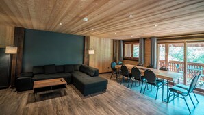 A modern interior with a wooden ceiling, a sectional sofa, a dining table with chairs, and a view of the outdoors.