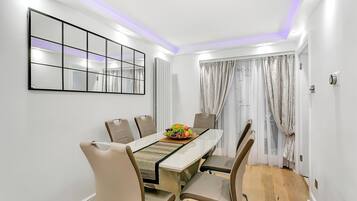 A dining area with a white table, beige chairs, a fruit bowl, and a mirror on the wall.