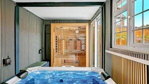 A spa room with a hot tub, wooden shelves, and a view of the outside.