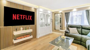 A modern living room with a flat-screen TV displaying 'NETFLIX', a fireplace, a sofa, and a coffee table.