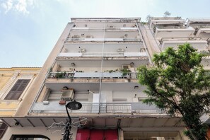 Un immeuble à plusieurs étages, doté de balcons et de climatiseurs, avec un arbre au premier plan.