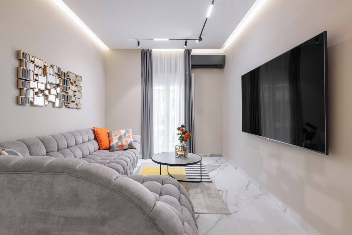 Een moderne woonkamer met een modulaire bank, een flatscreen televisie, een decoratief kunstwerk en een glazen vaas met bloemen.