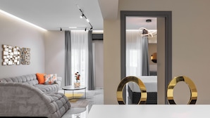 Een moderne woonkamer met een grijze bank, een bijzettafeltje en een eethoek met een witte tafel en gouden accenten.