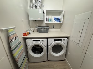 A compact laundry room with two front-loading washing machines, a small shelf with laundry supplies, and a towel rack. - *NEW Mid-Century Modern 2B/1B (Halifax)