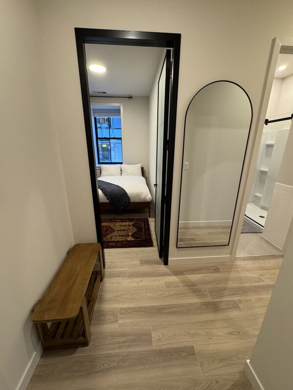 A narrow hallway leading to a bedroom with a bed, a bench, and a view of the outside. - *NEW Mid-Century Modern 2B/1B (Halifax)