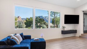 Un salón moderno con un sofá azul, ventanas amplias, un televisor de pantalla plana y suelo de madera.