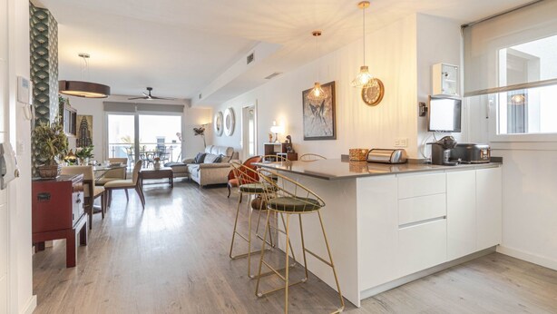 Uma cozinha moderna com ilha central, banquetas e iluminação pendente.