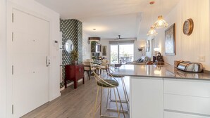 Uma cozinha moderna com armários brancos, uma ilha central, banquetas e iluminação pendente.