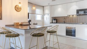 Cozinha moderna com armários brancos, eletrodomésticos de aço inoxidável e uma ilha central com banquetas.