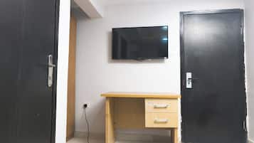 A room with a wooden desk, a black door, and a mounted TV.