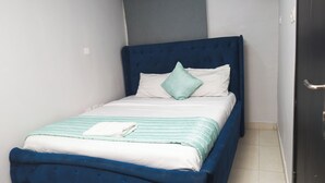 A single bed with a blue headboard, white bedding, and a green pillow.