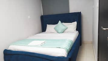 A single bed with a blue headboard, white bedding, and a green pillow.