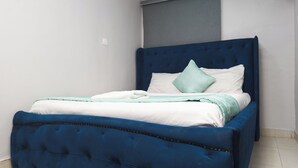 A bed with a blue headboard and white bedding, a light blue pillow, and a white blanket.