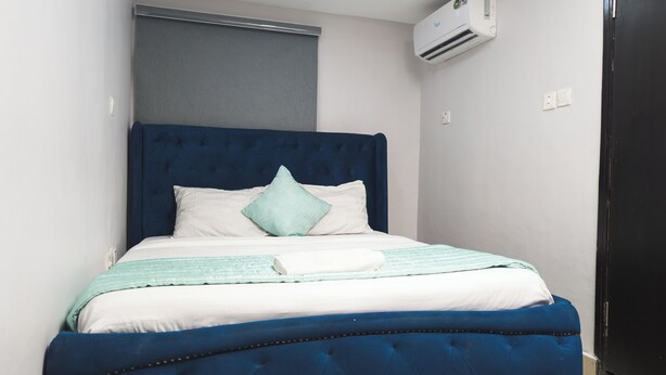 A bed with a blue upholstered headboard, white bedding, and a light blue throw blanket.