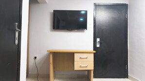 A room with a wooden desk, a television mounted on the wall, and a closed door.