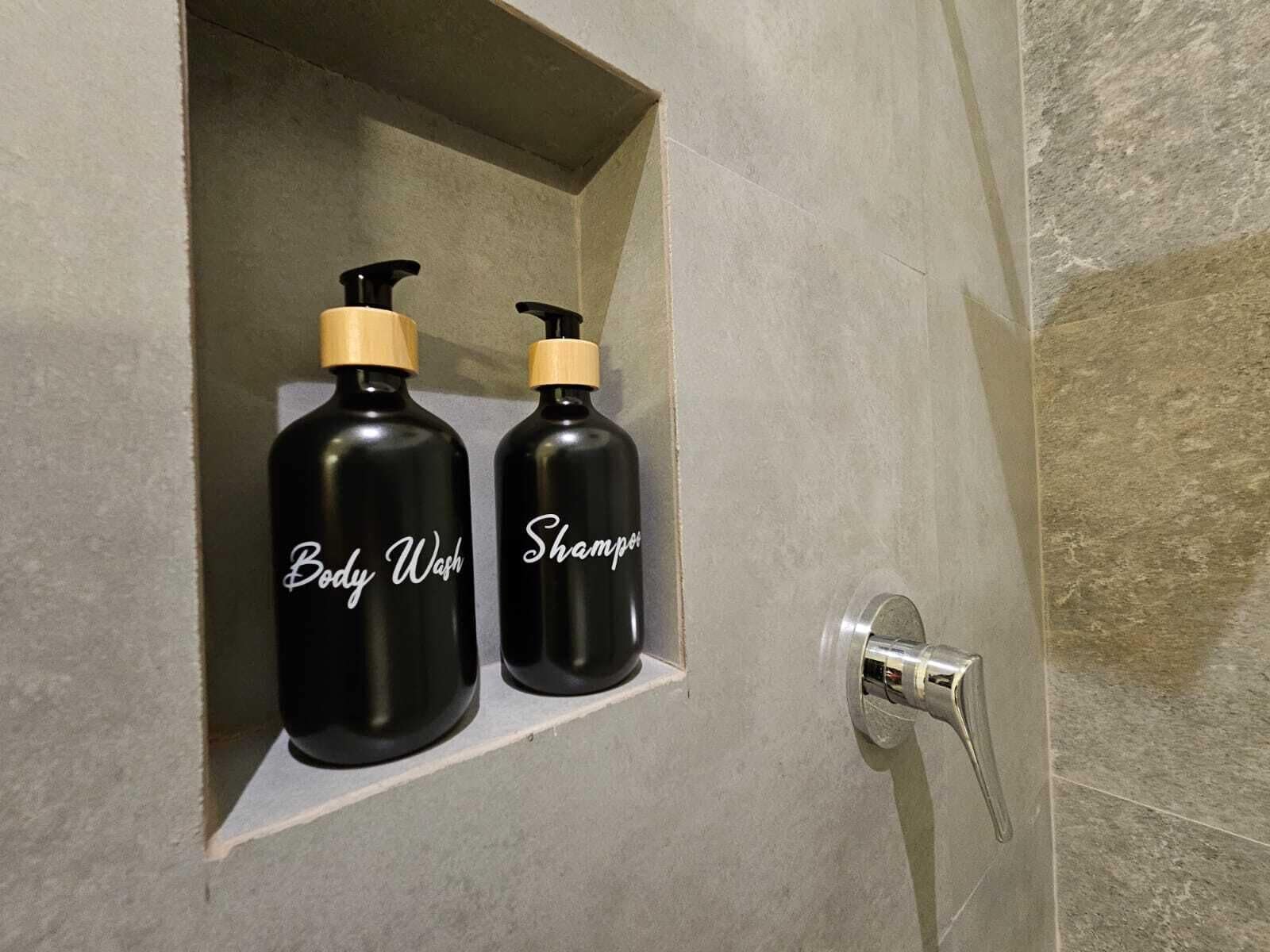 Un baño con un estante que contiene dos botellas negras etiquetadas como "Body Wash" y "Shampoo".