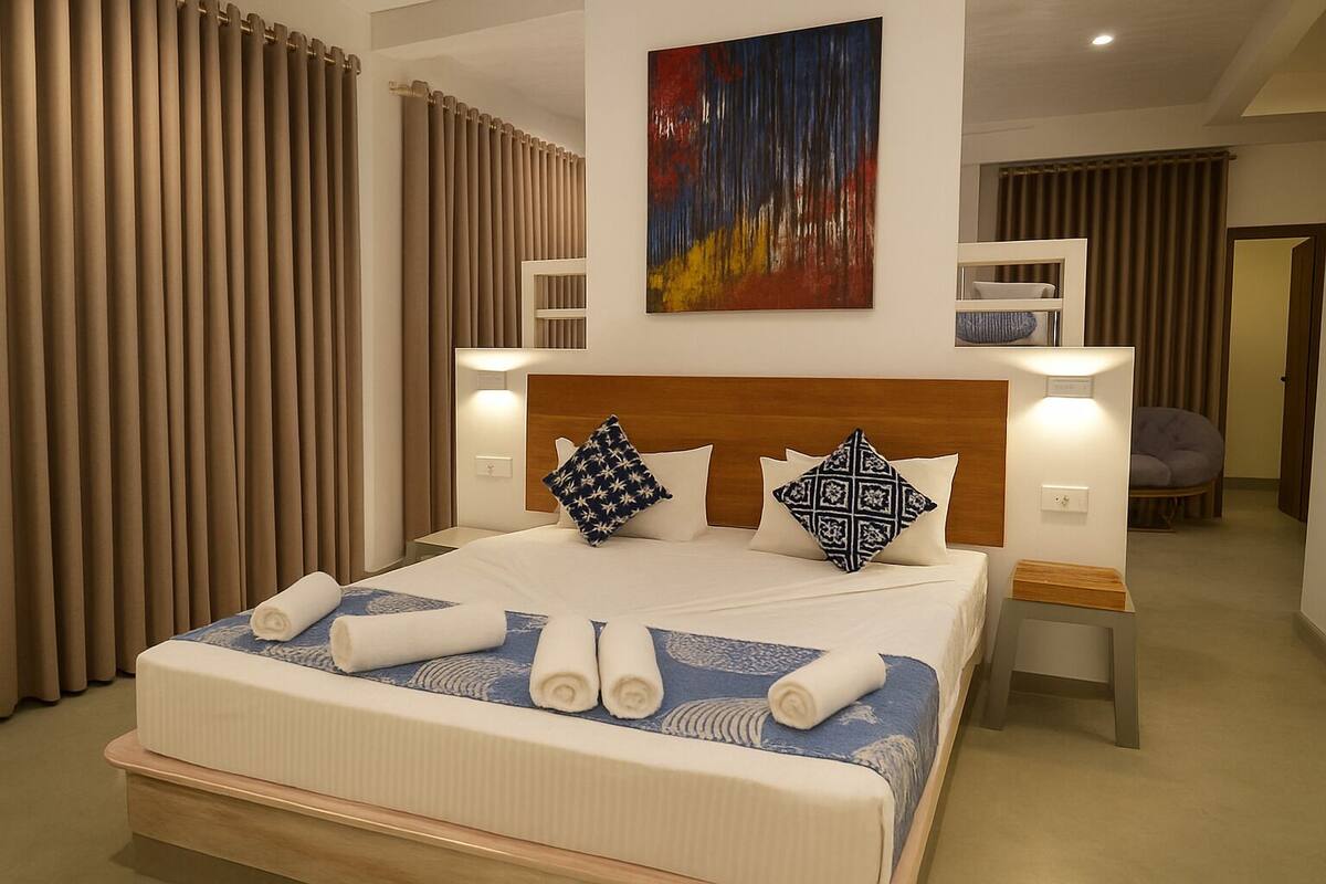 A neatly made bed with rolled towels, a headboard with a geometric pillow, and a painting above.