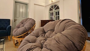 Ein Zimmer mit hohen Decken, einem großen Fenster und einem Korbstuhl mit Kissen.