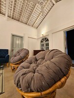 Quarto com teto alto, grande janela e cadeira de vime com almofada.