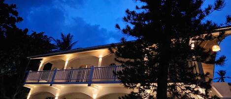 A two-story house with a balcony, arched windows, and a well-lit exterior at dusk.