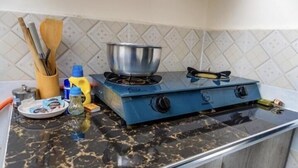 Una cocina con una estufa de gas azul, una olla de acero inoxidable, utensilios de madera y una encimera de mármol.