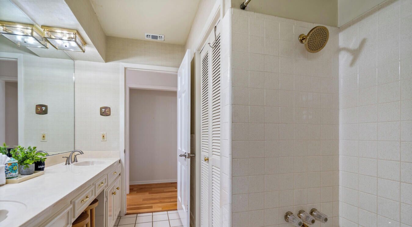 A bathroom with a white tiled shower, a sink with a mirror, and a door leading to another room.
