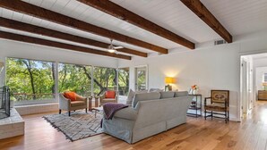 Un salon spacieux avec un canapé gris, un plancher en bois et de grandes fenêtres donnant sur la verdure.