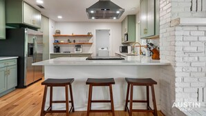 Une cuisine moderne dotée d’un îlot central, de tabourets de bar et d’un mur d’accent en briques blanches.