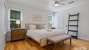 Une chambre à coucher comprenant un lit, des tables de chevet, un banc, un ventilateur de plafond et une échelle.