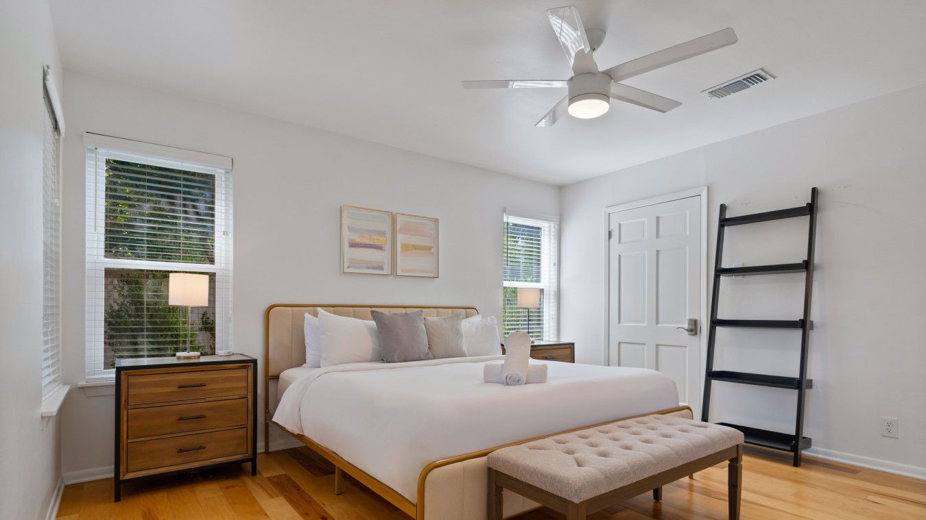 A bedroom with a bed, bedside tables, a bench, a ceiling fan, and a ladder.
