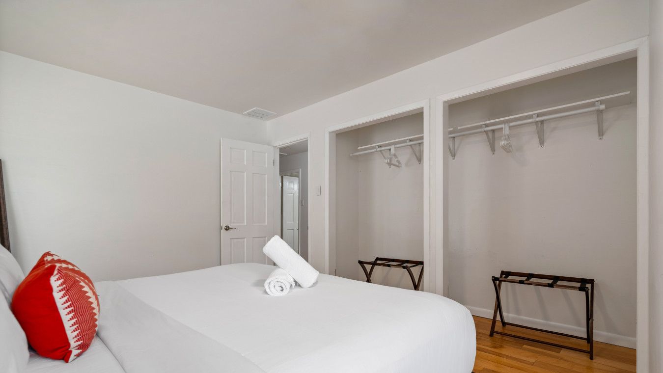 Un dormitorio con una cama grande, un cojín rojo, una toalla blanca y suelo de madera. Hay dos armarios con barras para colgar.