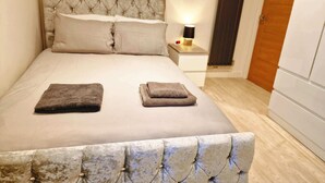 A neatly made bed with two folded towels, a bedside lamp, and a wooden door in a hotel room.