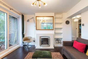 Een moderne woonkamer met een open haard, een bank, een fauteuil en een groot raam.