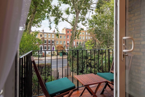 A balcony with a view of a row of townhouses, a wooden table, and two green cushioned chairs.