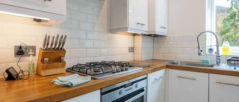 A modern kitchen with white cabinets, a gas stove, an oven, and a window with a view of greenery outside.