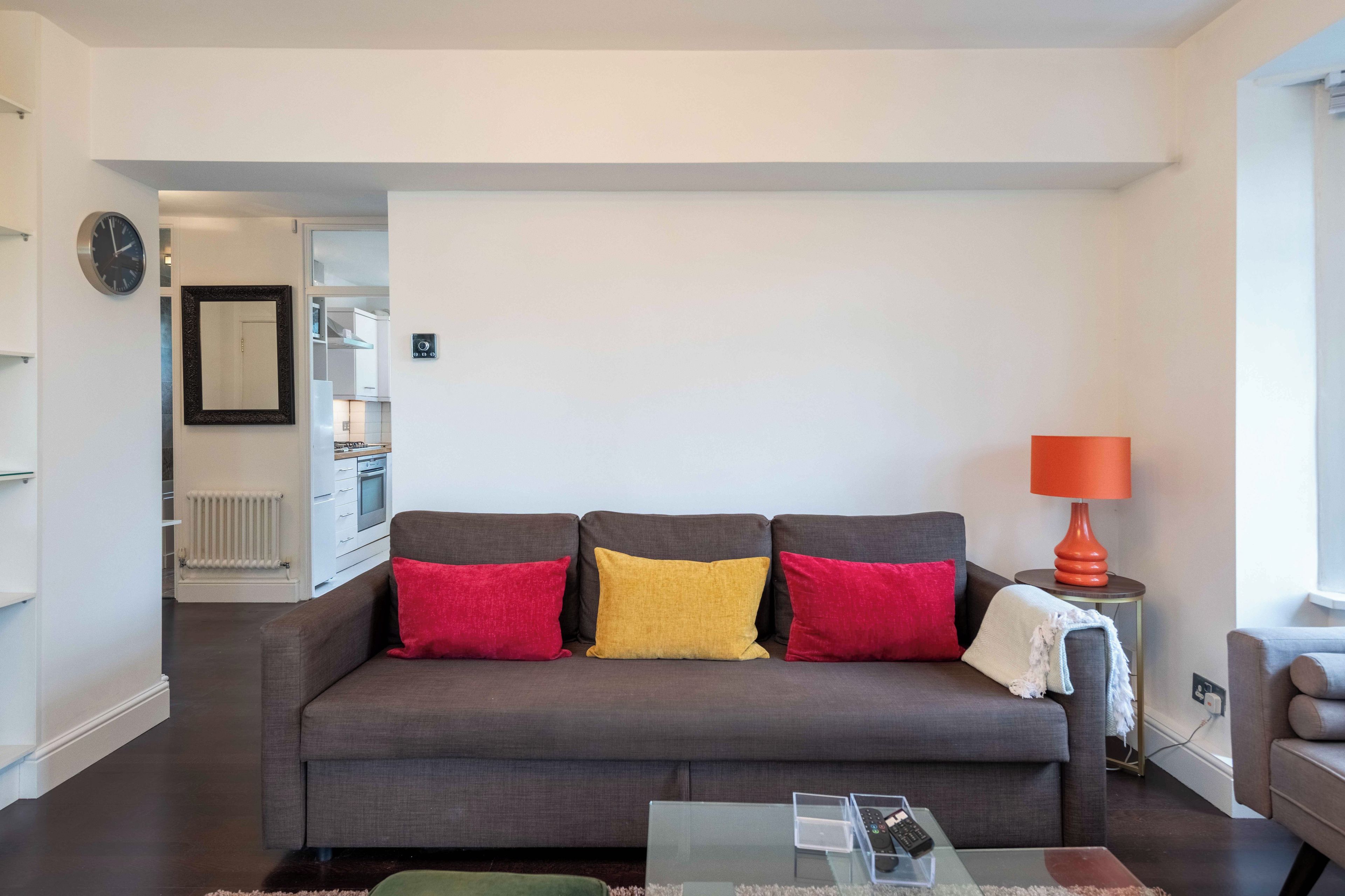 Una sala de estar moderna con un sofá gris, una mesa de centro de vidrio y una lámpara roja.