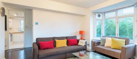 A modern living room with a sofa, armchairs, a glass coffee table, and a dining table.