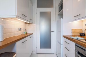 Een moderne keuken met witte kasten, een houten aanrecht en een matglazen deur.