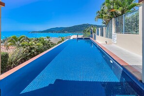 Ein Swimmingpool mit Blick auf das Meer und eine Hügelkulisse im Hintergrund.