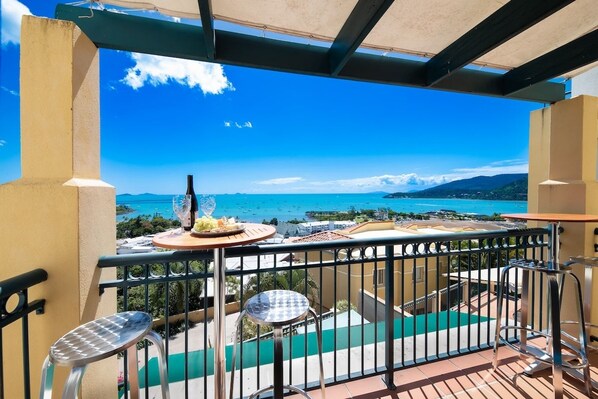 A balcony with a table set for two, overlooking a coastal view.