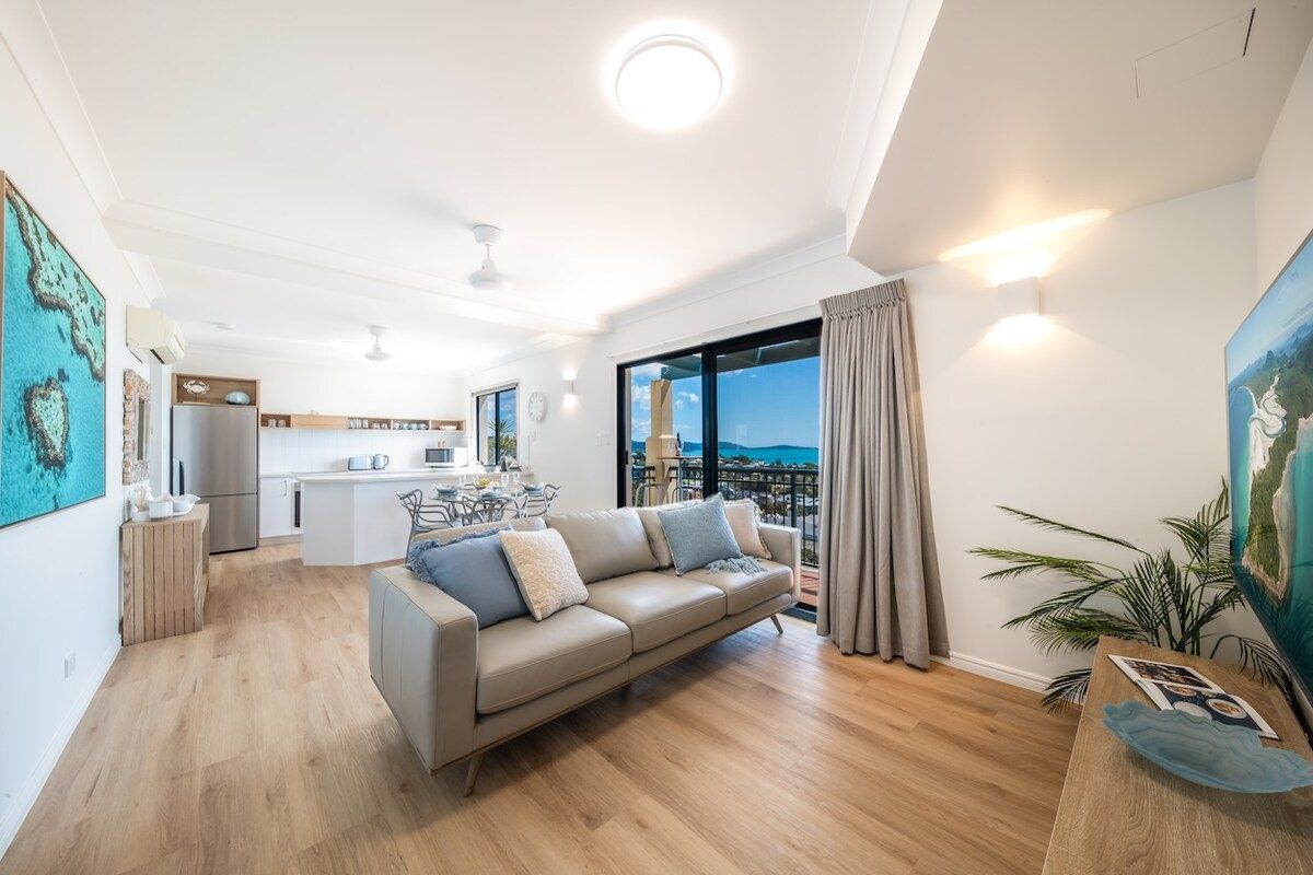 A modern living room with a sofa, a dining area, and a kitchen.