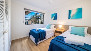 Habitación de hotel con dos camas, una ventana que da a palmeras y obras de arte en las paredes.